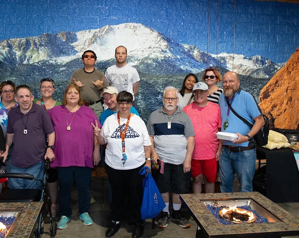 A group of adults smiles in front of a mural of Pikes Peak.